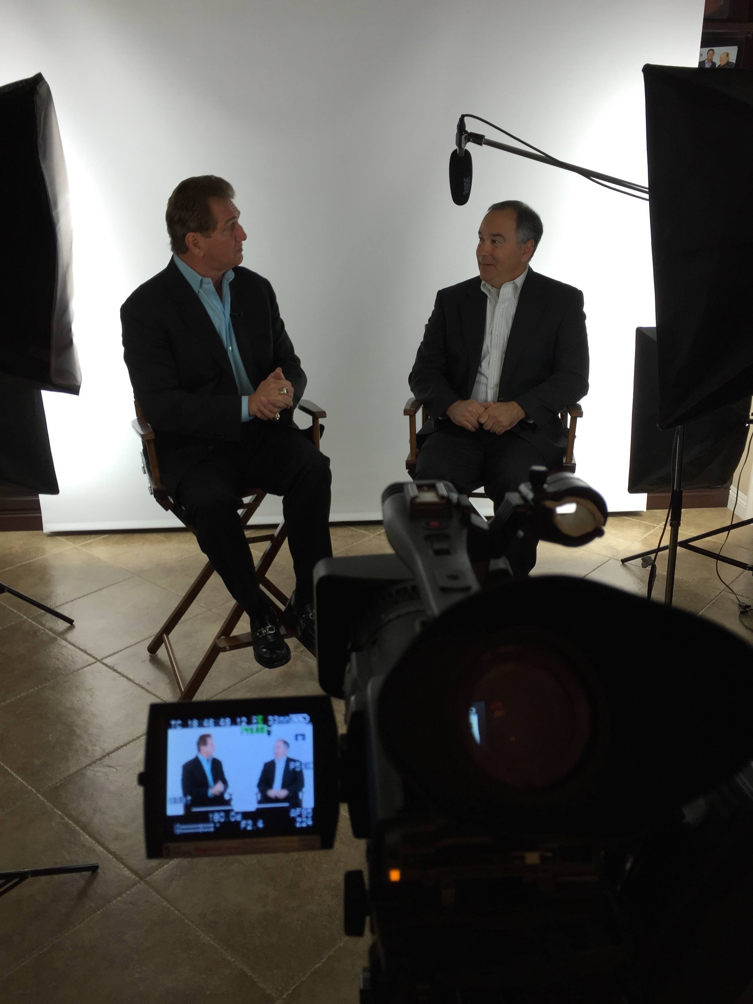 Two men sitting in chairs in front of a camera.