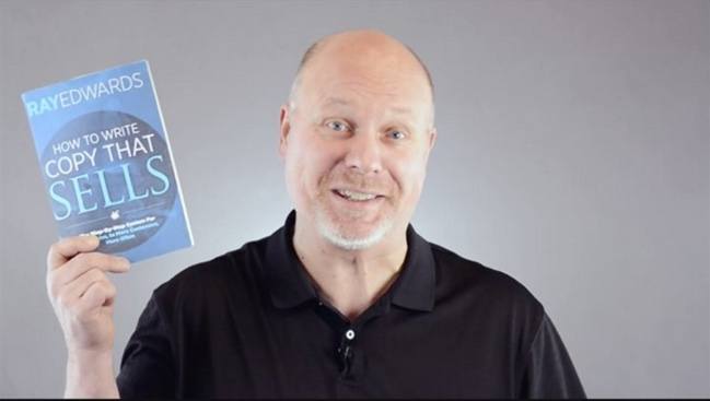 A bald man holding up a book that sells.